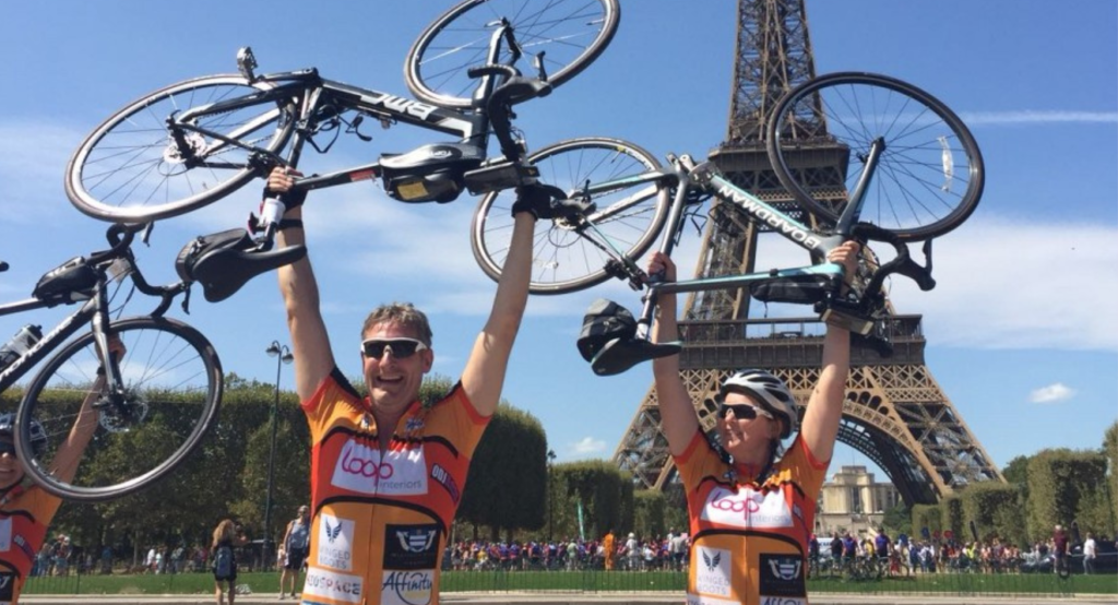 Two cyclists holding their bikes aloft next to the Eiffel Tower