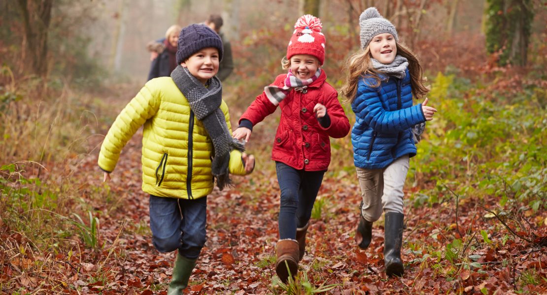 Three children running happily through a forest