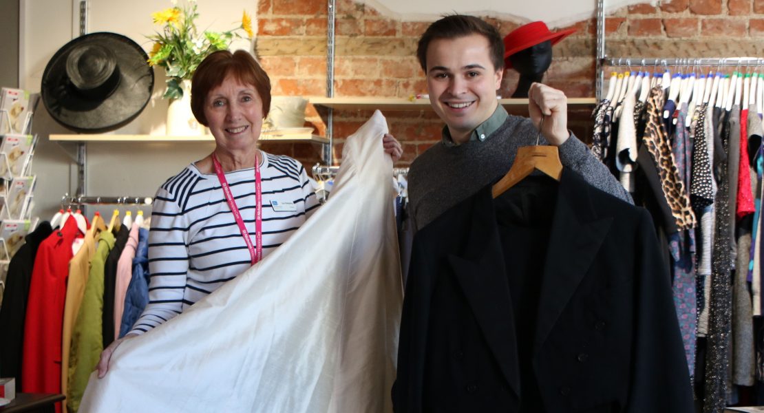 Retail staff and volunteer holding up wedding dress and suit