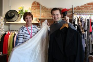 Retail staff and volunteer holding up wedding dress and suit