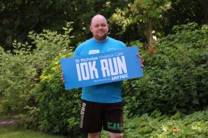 Hospice Fundraiser Lee Graham holding a sign advertising that he will be taking place in the Hospice's 10K event