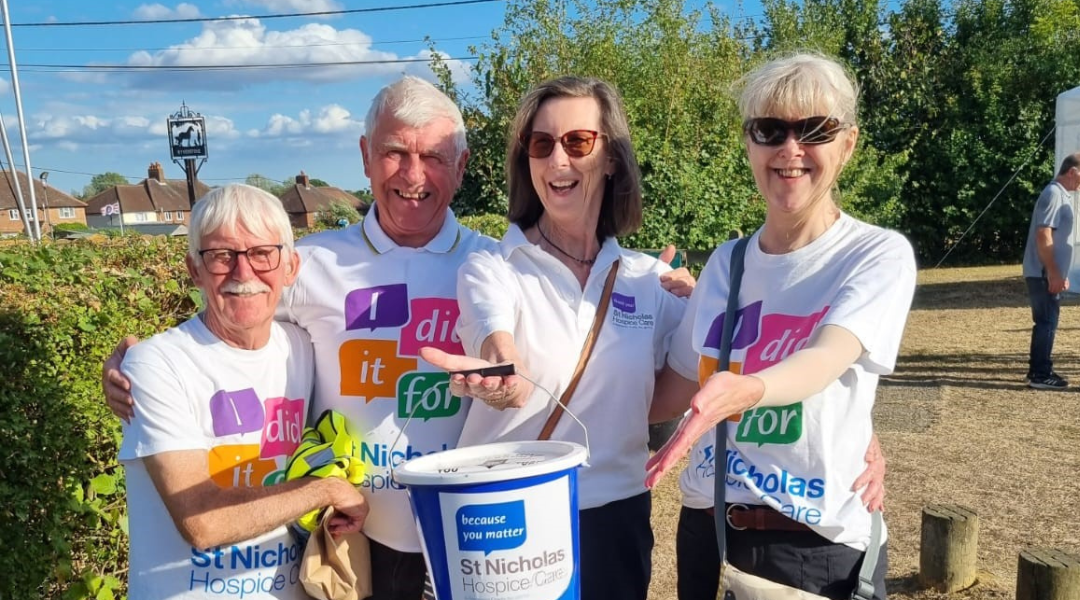 Image of four St Nicholas Hospice Care volunteers holding up a donation bucket and pointing at it