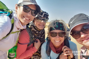 Group of people smiling wearing sunglasses, dressed for a trek, in desert surroundings