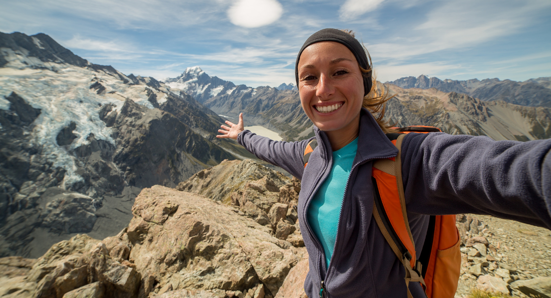 A woman smiling with arms outstretched standing on top of a mountain