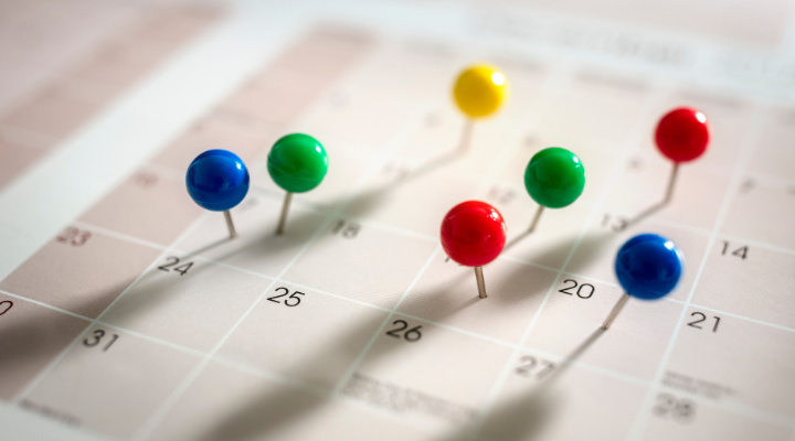 A close up image of a calendar with pins in some of the dates