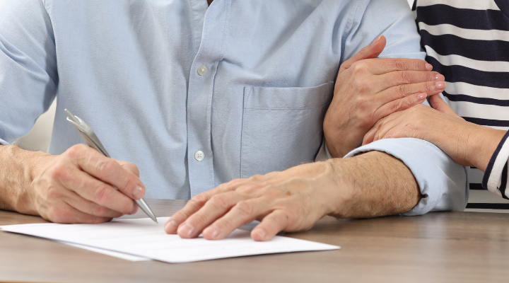 Someone signing a Will whilst the person next to them holds their arm