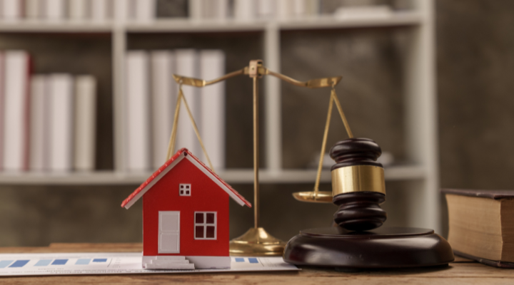 A pair of weighing scales with the model of a house on one side and a gavel on the other