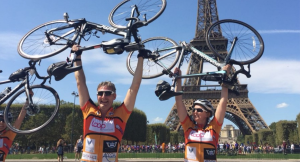 Two cyclists holding their bikes aloft next to the Eiffel Tower