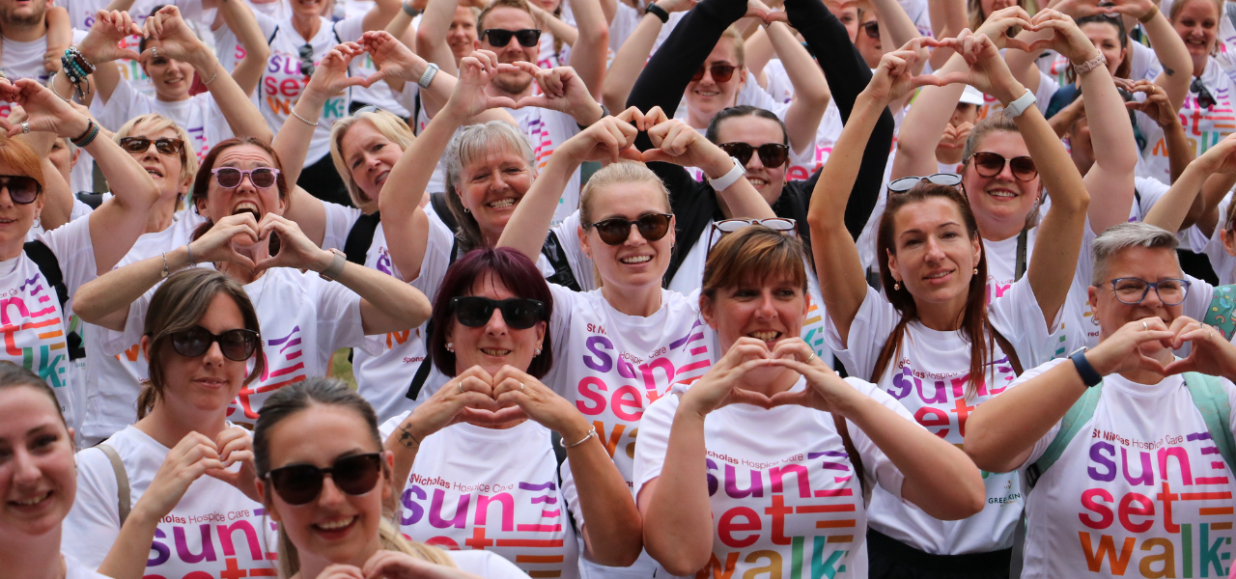 Crowd of smiling Sunset Walk participants wearing Sunset Walk t-shirts and making heart shapes with their hands