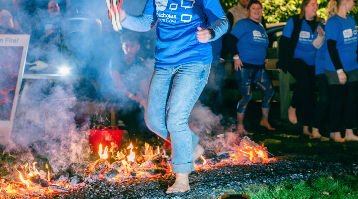 person walking on hot coals wearing a St Nicholas Hospice Care t-shirt, with other participants smiling in the background
