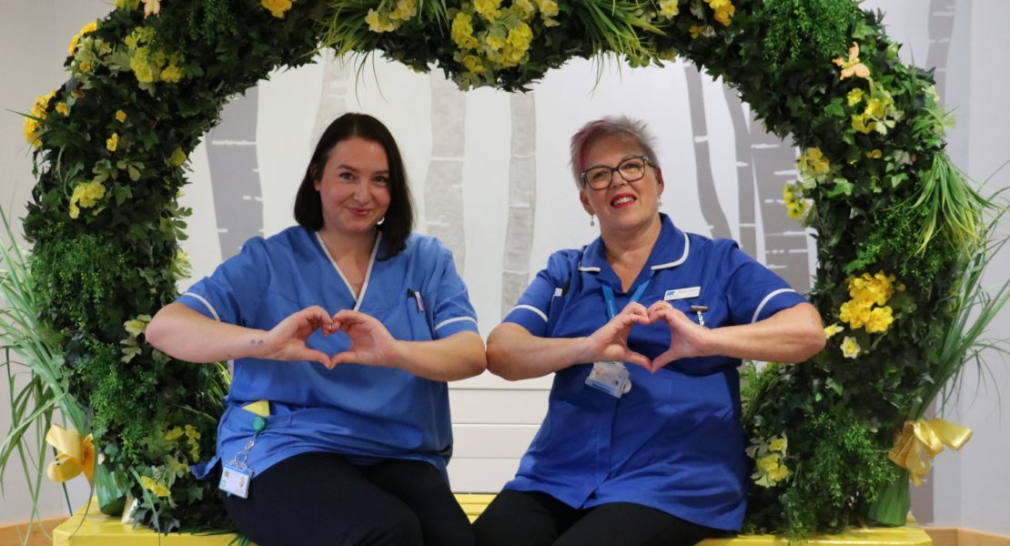 two hospice nurses posing in a flower wreath with hands in the shape of hearts