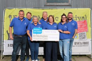 A group of people waring blue t-shirts smiling holding up a large check which states £21,000 has been raised