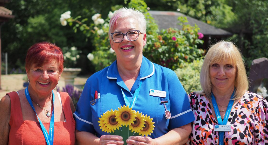Hospice nurse and staff in garden holding sunflower memory and smiling to camera