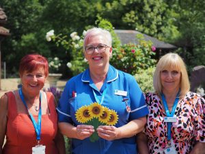 Hospice nurse and staff in garden holding sunflower memory and smiling to camera