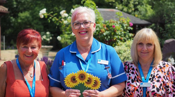 Hospice nurse and staff in garden holding sunflower memory and smiling to camera