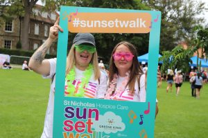 Sunset Walk participants wearing neon sunglasses smiling through the selfie frame