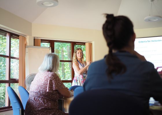 Trainer delivering an educational presentation to attendees in a meeting room with a projected slide and flip chart.