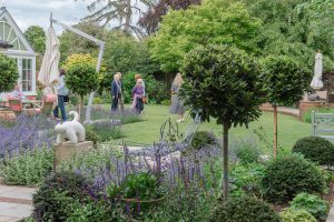 Visitors exploring a landscaped private garden with colourful flower beds, trimmed trees and lawn during the Hidden Gardens of Bury event.